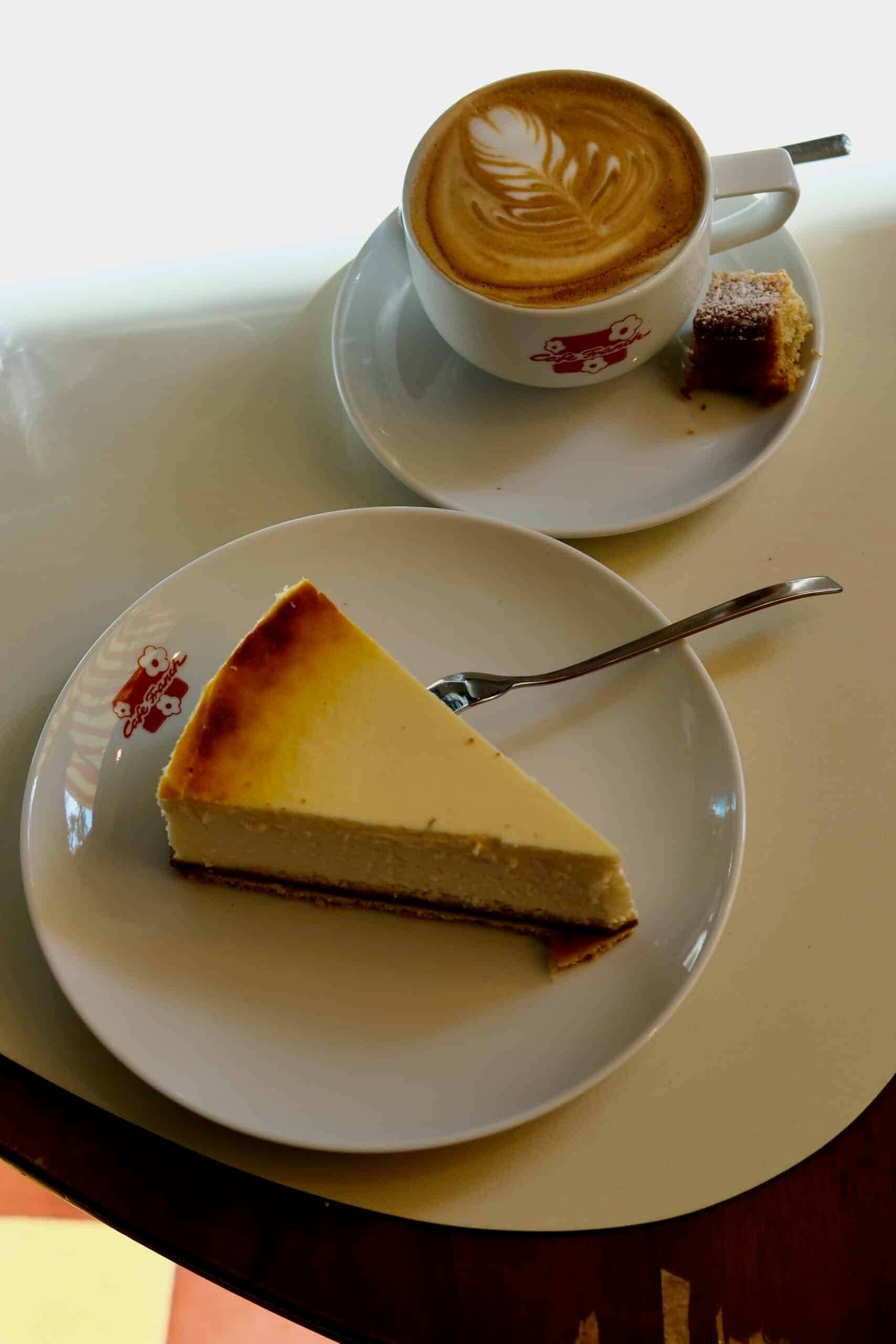 Teller mit einem Stück Käsekuchen, daneben ein Cappuccino mit Latte Art, aufgenommen im Café Franck