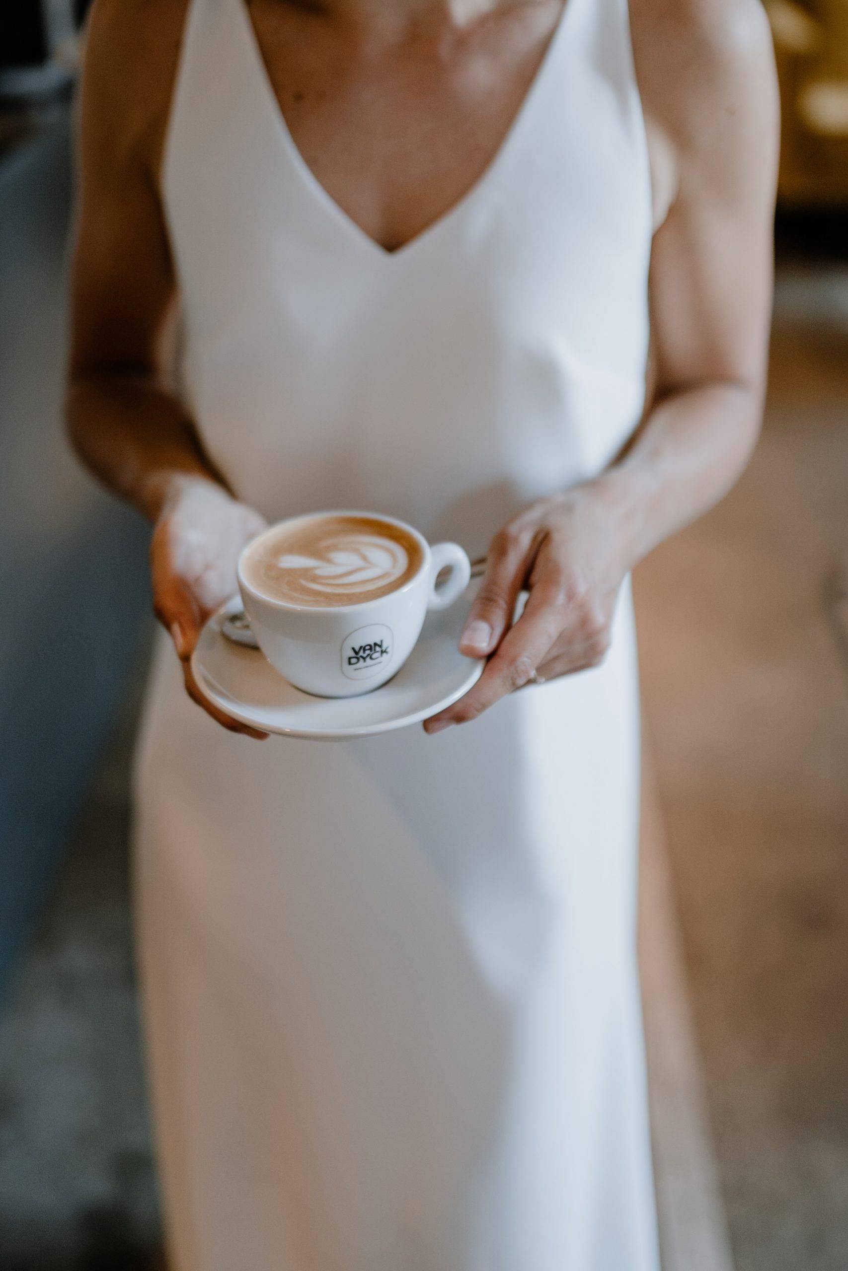 Eine Frau in einem weißen Kleid hält eine Tasse mit Latte Art in der Hand