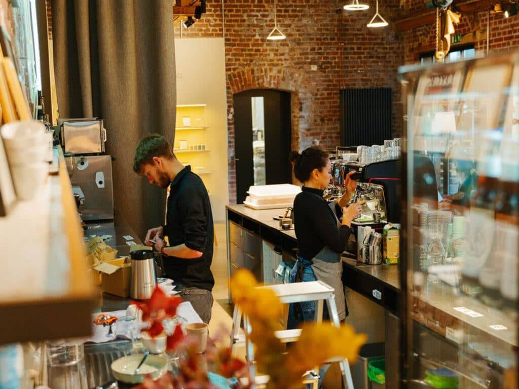 Eine Baristi bereitet Kaffee zu, ein weiterer Barista räumt auf.