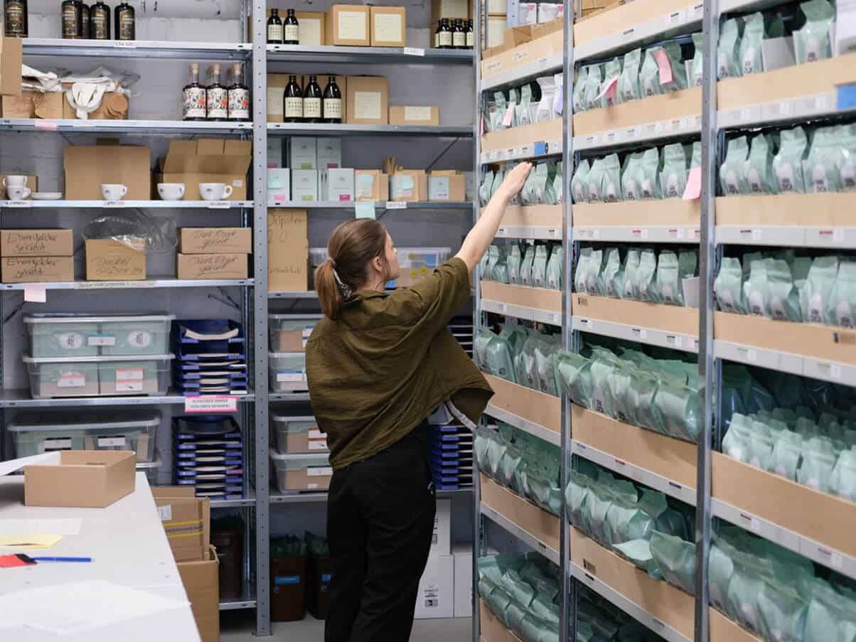 Eine Mitarbeiterin greift in das Lagerregal nach einem Kaffeepaket