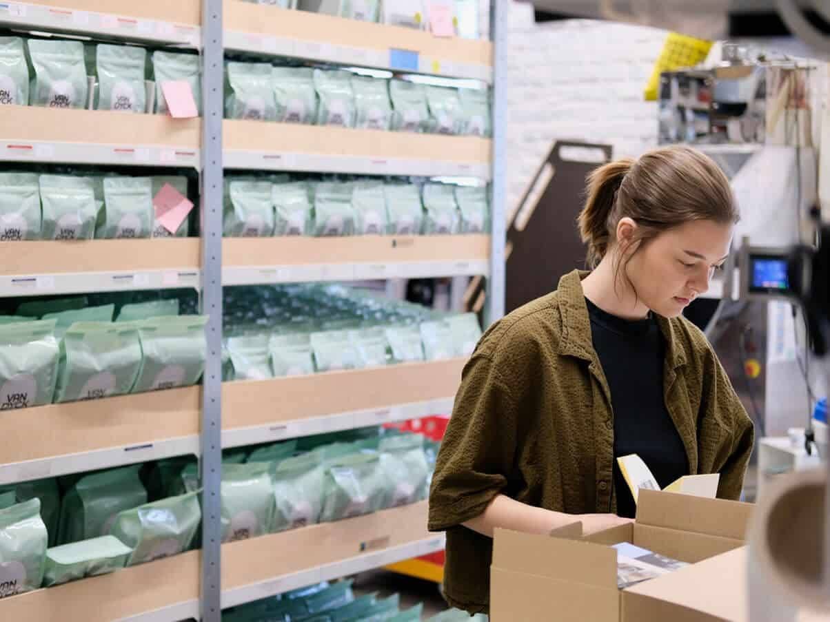 Eine Mitarbeiterin steht in der Lagerhalle und packt ein Paket